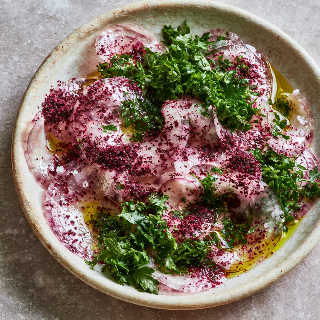 Close-up of flaky sea salt and burgundy sumac powder on thin onion slices.