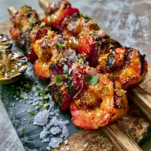 Top-down view of glistening grilled margarita shrimp kebabs with lime-tequila glaze and micro-cilantro.