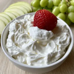 Top-down view of a matte white bowl with whipped fruit dip recipe surrounded by apples and grapes.