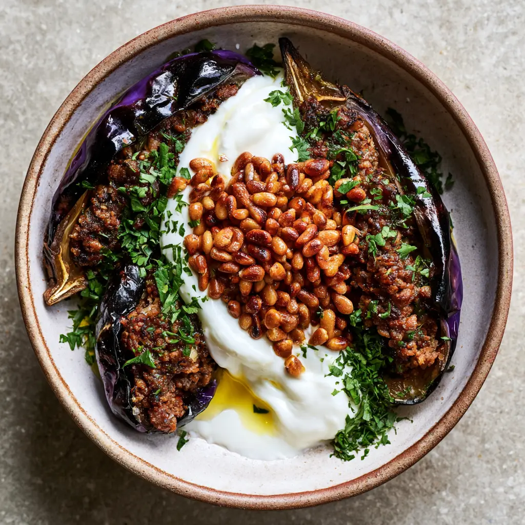 Detailed view of snowy white garlic yogurt sauce draped over stuffed eggplants with emerald green parsley. (Sheikh El Mahshi recipe)