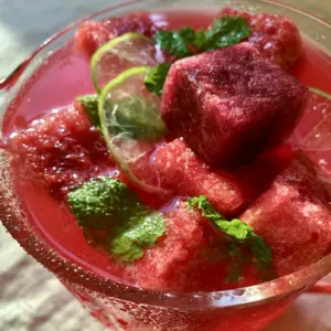 Top-down extreme close-up of vibrant red watermelon punch with geometric frozen cubes and mint leaves.