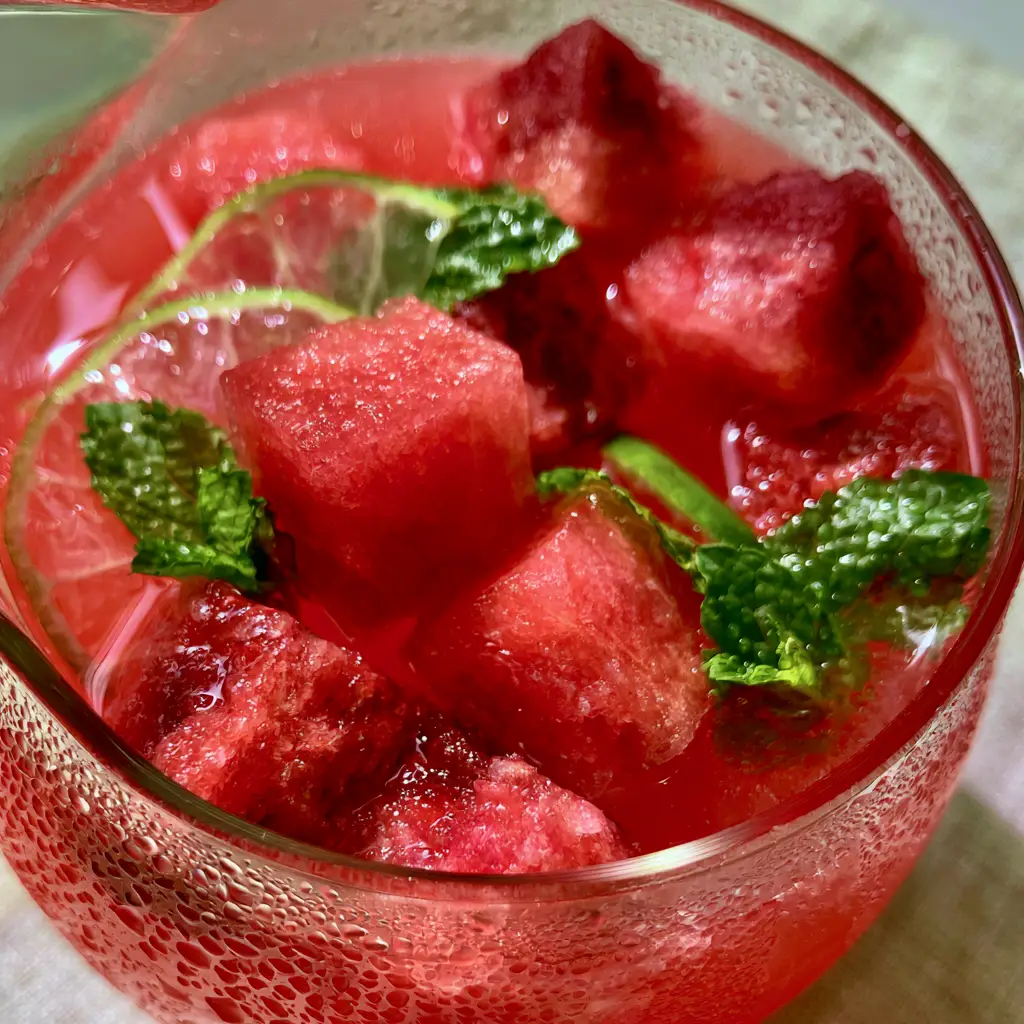 Macro view of heavy condensation droplets on a chilled glass pitcher filled with bright red punch.